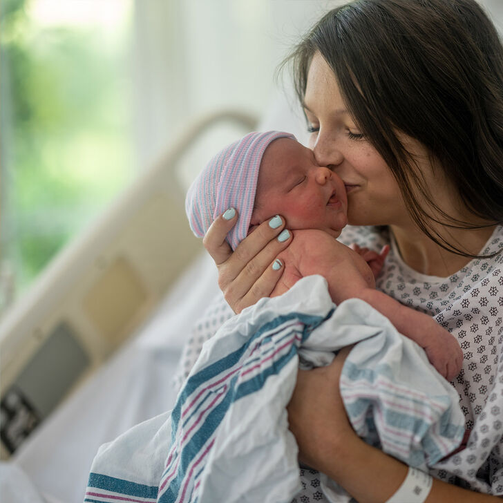 A mother kisses her newborn baby in a delivery room