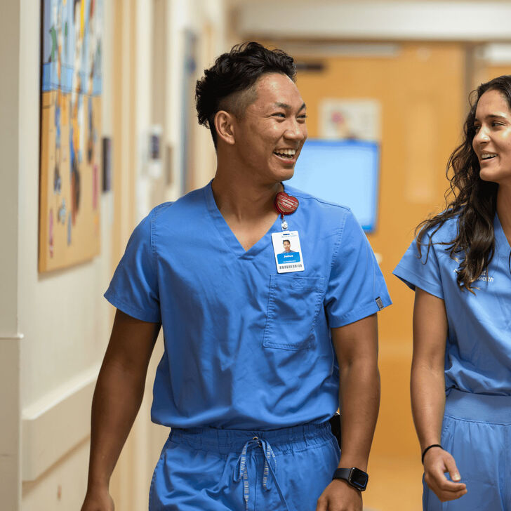 A young male and young female nurse walk down a hospital hallway together