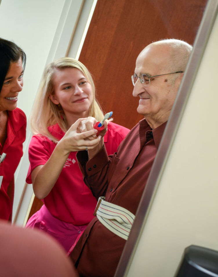 Image of faculty member smiling and helping patient with a student