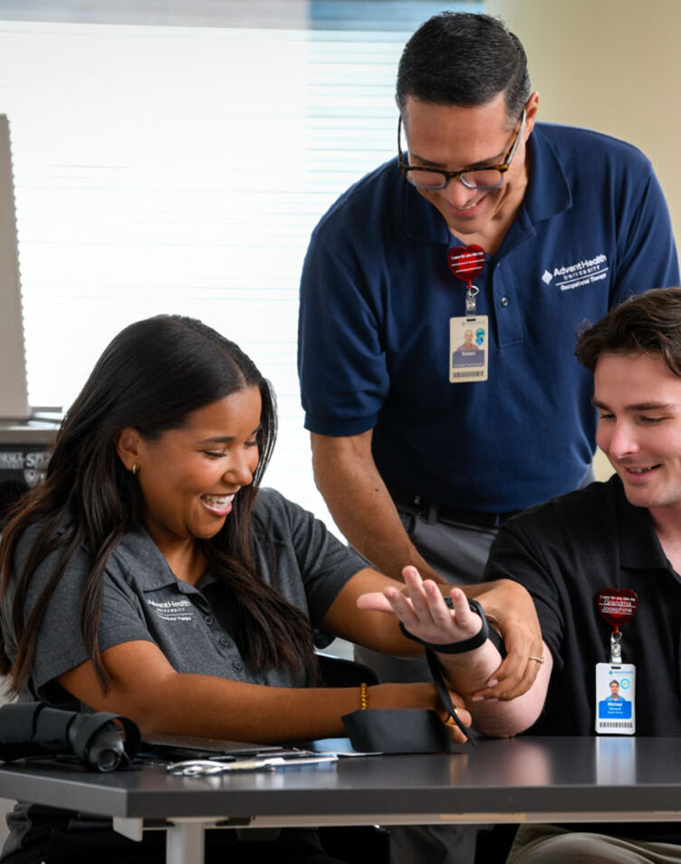 Image of faculty member smiling and helping two students with a hand therapy machine